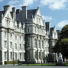Photograph of a tall and wide grey building with a pointed roof and lots of rectangular windows.