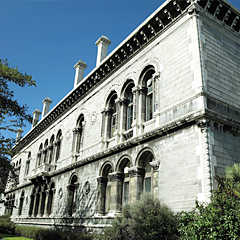 Photograph of a long grey building with arched windows and chimneys on the roof