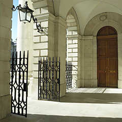 Photograph of a porch with an arched wooden door leading into the interior and arches leading outside. The interior arches have black iron gates.
