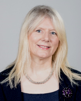 A Headshot of Dr Eilish Burke wearing a purple jacket and a silver necklace.