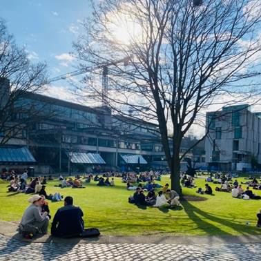 A group of people sitting on the grass in front of a building  Description automatically generated with medium confidence